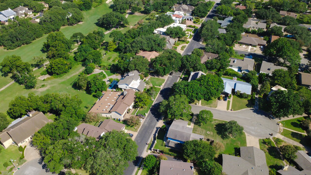 Winding roadways throughout Onion Creek subdivision loop past rooftops in Austin suburban neighborhoods. Mature trees canopy peaceful streets adjoining golf fairways near Pebble Beach Drive