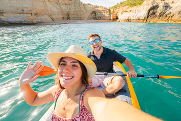 Young couple enjoying a summer adventure, paddling an inflatable kayak in turquoise ocean water...