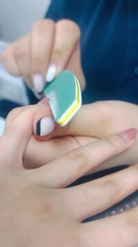 Woman filing toenail with blue nail file close up 9:16 vertical, pedicure nail care beauty salon concept