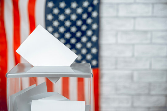 Voting ballot entering a transparent voting box with the US flag in the background, symbolizing American elections and democracy.