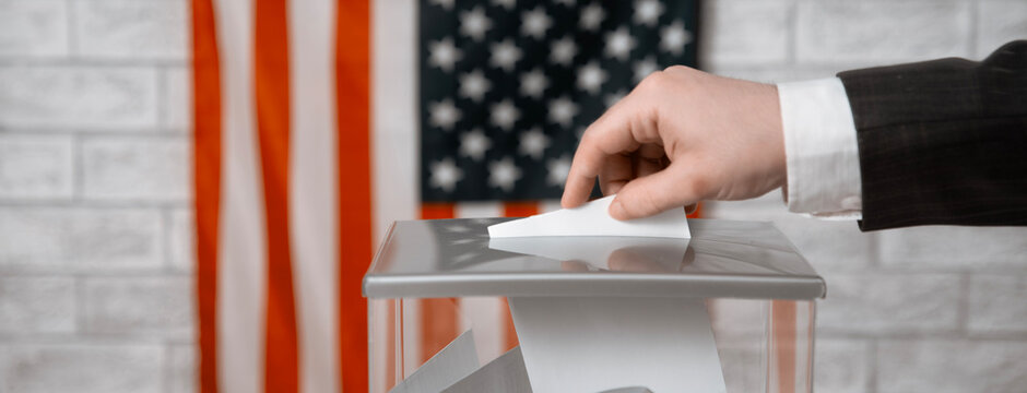 Voter casting a voting ballot into a transparent ballot box with the US flag. American elections, democracy and voting rights.
