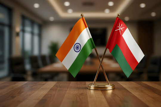 Miniature flags of india and oman displayed on a wooden desk in a blurred office environment, representing international diplomatic relations