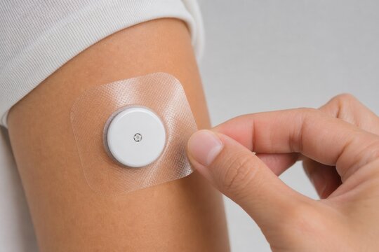 Hand applying adhesive patch over glucose sensor on arm