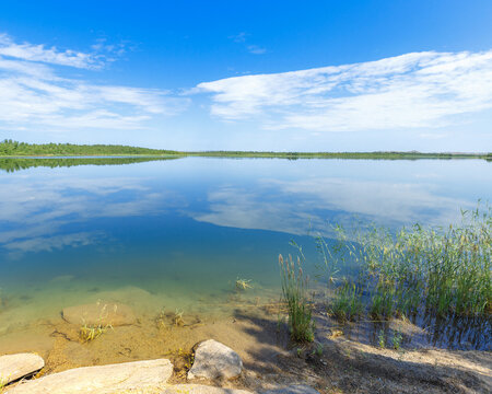 Stony shore lake Ulken Shabakty with blue water and reflection of green plants and blue sky with white clouds. Beautiful scenic landscape in Burabay National Nature Park. Summer nature travel photo.