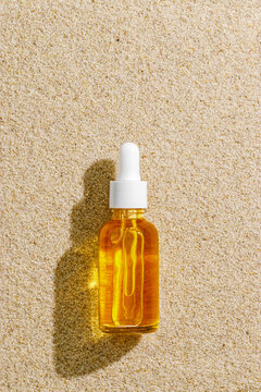 Top view glass dropper bottle with yellow golden liquid essence, serum on beach sand beige background, beautiful sunlight shadow. Natural Cosmetic, aesthetic mock up after sun summer cosmetic product.