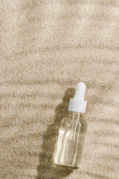 Glass dropper bottle of clear liquid essence, deep hydration serum on beige sand at sunlight, leaf shadow. Mock up skin care product. Eco beauty concept of natural cosmetics, organic botanical extract