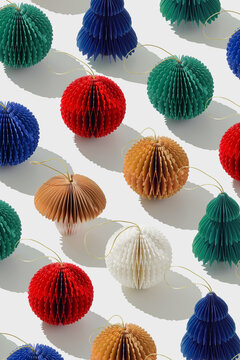 Colorful Paper Christmas Ornaments as round balls and Christmas trees, hanging crafted eco-friendly New Year decor. Minimal aesthetic holidays repeat pattern, top view background of winter baubles.