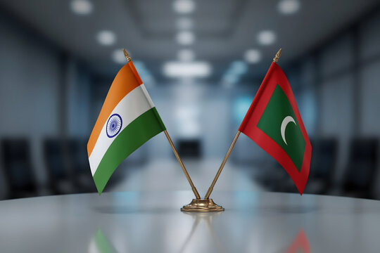 Small flags of india and maldives placed on a table in a blurred conference room, representing international diplomacy and state relations