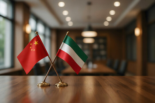 Two small table flags of china and kuwait crossed on a wooden desk in a blurred meeting room with soft warm lighting and dark background