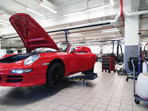 Moscow, Russia - July 30, 2026: Classic red Porsche 911 sports car in a service center. Car maintenance and repair are being carried out. The car is on a lift, and the hood is open. Selected focus.