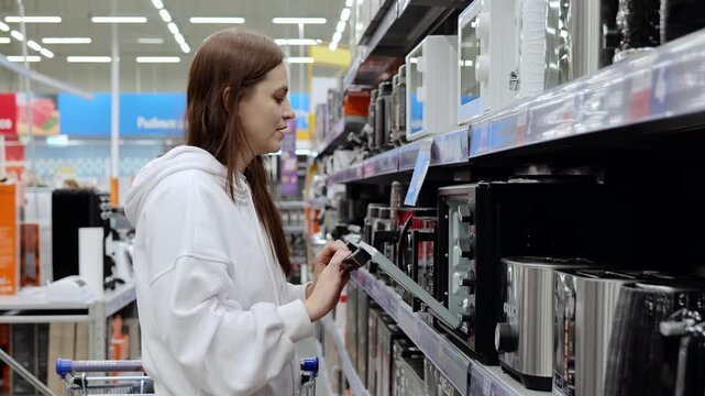 Young woman choosing new microwave oven in a home appliance store. Electronics retail store with consumer electronics products