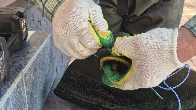 Gardener installing nylon cutting line into grass trimmer head. Maintenance and repair of string trimmer tool. Outdoor landscaping equipment preparation concept.