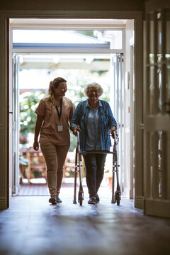 A professional caregiver walking gently alongside an active senior. The senior is using a modern, lightweight mobility aid.