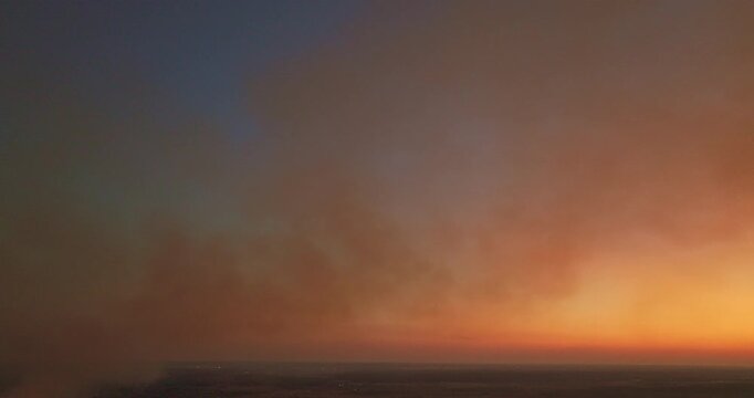 Aerial view of Smoke from burning fields spreads across the rural sky, slowly erasing the colors of sunset and turning a peaceful evening into a sign of environmental harm.