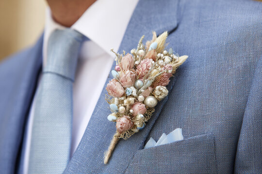 Groom inspired pastel dried flower brooch pinned to blue suit lapel for wedding boutonniere background and menswear styling detail
