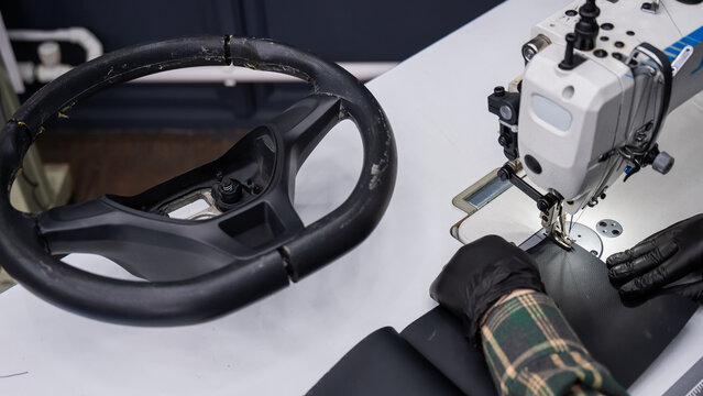 A seamstress in a workshop makes a new leather cover for a car steering wheel.