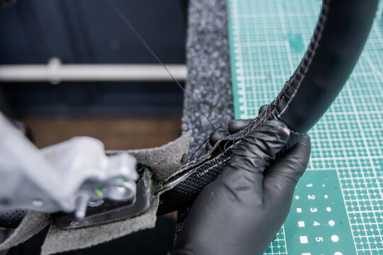 A seamstress in a workshop makes a new leather cover for a car steering wheel.
