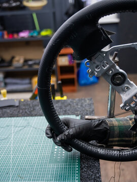 A seamstress in a workshop makes a new leather cover for a car steering wheel.