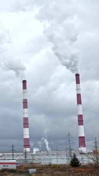 Two tall. Red and white industrial chimneys billowing thick smoke and steam into a grey. Overcast sky. Highlighting the concepts of air pollution and global warming from fossil fuel energy production