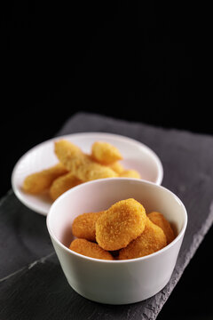 Golden chicken nuggets in white bowls on slate surface, top view