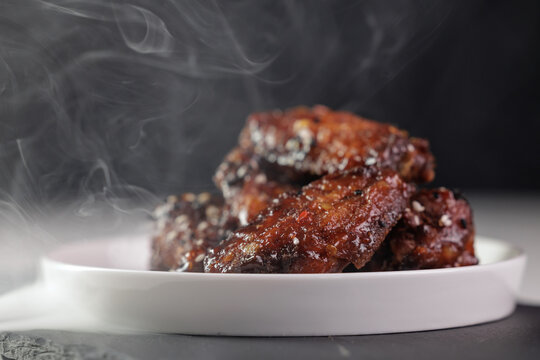Steaming hot glazed barbecue chicken wings on white plate