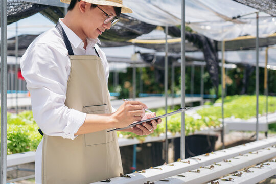 A man wearing a white shirt and apron is writing on a clipboard