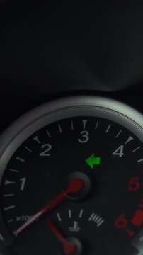 A driver activates the left turn signal on a car dashboard, the illuminated arrow visible in a close-up of the passenger-vehicle instrument panel with the ignition on, showing a routine control check