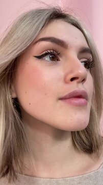 Young girl Posing for Camera with black Winged Eyeliner Makeup. Woman doing everyday casual makeup, drawing black eyeliner, eyeshadow, applies winged eyeliner to eyes. Vertical mobile ugc video