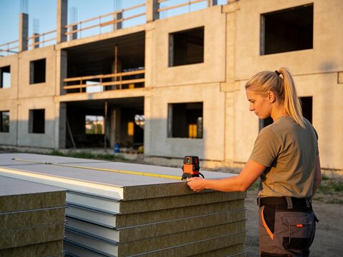 Blonde female construction engineer uses precision laser leveling device for accurate measurements at outdoor building site