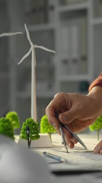 A fair-skinned European architect-engineer plans wind turbine locations, developing a sustainable city concept using scale models in a bright, well-lit design laboratory setting
