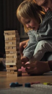 A family of parents and their daughter sit on the living-room floor of their home, playing a board game together, the scene shows a relaxed domestic atmosphere and a sense of unity