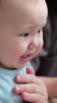 Emotional close up portrait of a crying newborn baby with tears in her eyes and a sad face, feeling upset and unhappy while her mother's hands gently comfort her