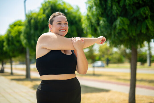 Plus size woman stretching arm outdoors in park