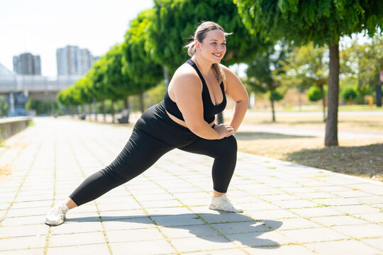 Plus size woman stretching legs in park