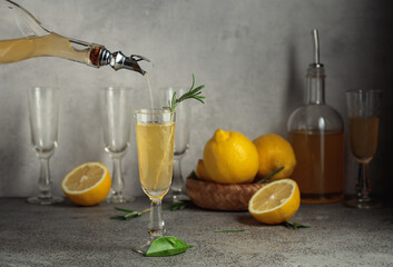 Obraz premium Italian liqueur Limoncello with fresh lemons and rosemary branches on a gray stone table.