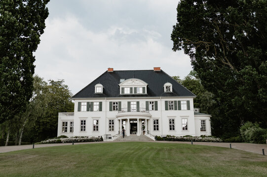 Elegant white manor house with a symmetrical facade behind a manicured lawn.