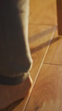 A person walks barefoot across a smooth wooden floor, morning light streams in through a window, illuminating the floor's grain and creating a relaxed atmosphere in the quiet space