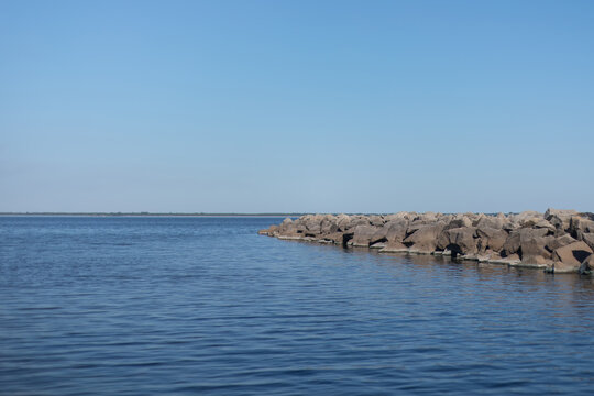 Minimalist summer landscape with calm lake, rocky breakwater and wide blue sky copy space