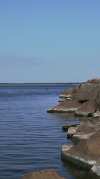 Vertical rocky breakwater beside tranquil blue water with copy space