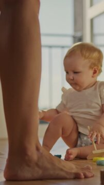 A young girl sits on the floor, focused on her game, while her mother walks smoothly around the room, the camera shows a close-up of the child's bare feet as she moves, in a calm home setting