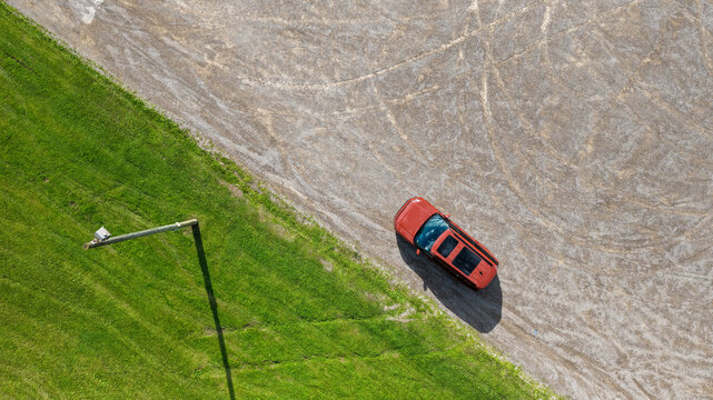 Red car parked on gravel next to green grass