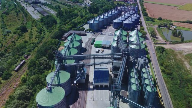 Dynamic high angle overview captures rows of steel grain silos with green and silver roofs at modern agricultural infrastructure plant.