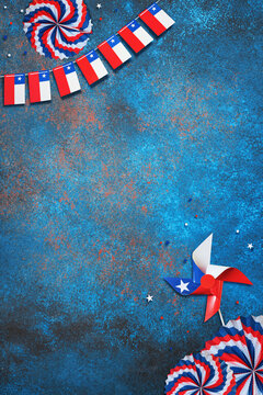 Chilean flag bunting, pinwheel, and paper fans decorating a textured blue surface for a national celebration