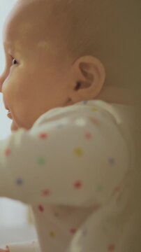 An happy baby reaches his hand through the bed railing toward his parents, who sit nearby, while soft daytime light streams across the bedroom, the room appears gentle, warm, and cozy