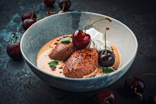 Modern dessert - dark black chocolate mousse au chocolat in vanilla sauce with black sweet cherries and meringues served as close-up in a design bowl