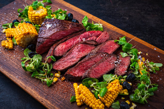 BBQ roasted under-blade steak chuck roast, denver cut beef steak with grilled vegetables, maiz corn, green salad served as close-up on a wooden board