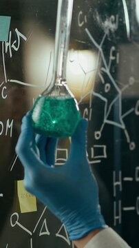 Middle-aged doctor in sleek research center holds clear test tube, studying swirling chemical liquid of ongoing experiment. He peers at the sample, noting its color and reaction under lab lighting
