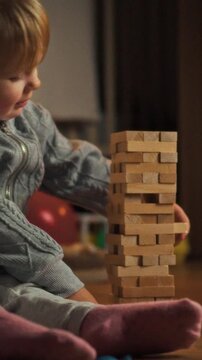 Mother and daughter sit on floor, stacking wooden blocks to raise tall tower, their hands alternating placements as they play, illustrating shared evening activity focused on building and cooperation