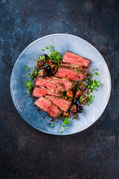 Traditional barbecue grass-fed dry aged roast beef steak tagliata with grilled mushrooms, fresh greens and herbs served as top view on a design plate - meat food recipe