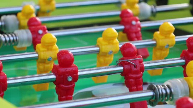 Close up of red and yellow plastic players on table football foosball board game outdoors. Tabletop soccer game with metal rods and miniature figures, recreation and leisure activity concept.